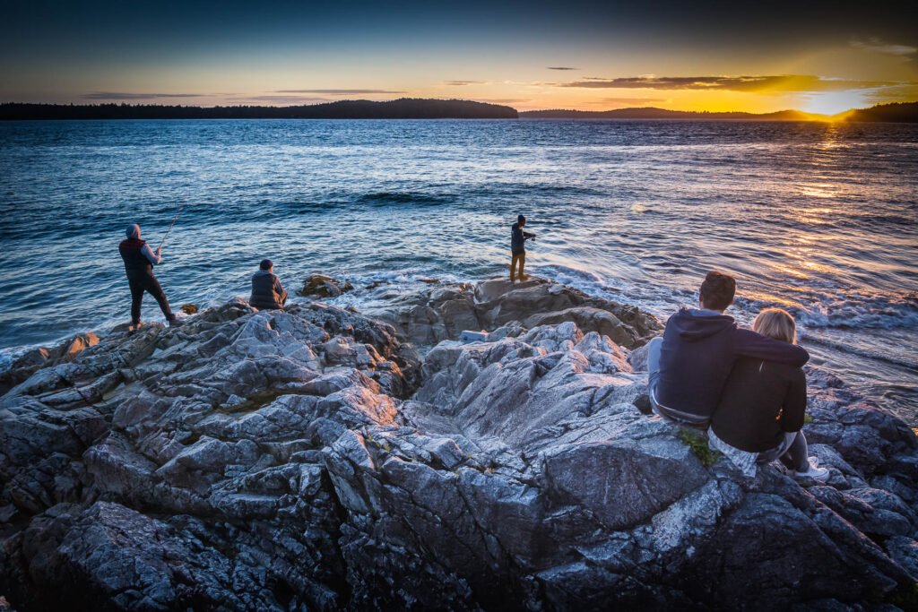 Menschen sitzen und angeln auf Felsen an der Küste von British Columbia bei Sonnenuntergang