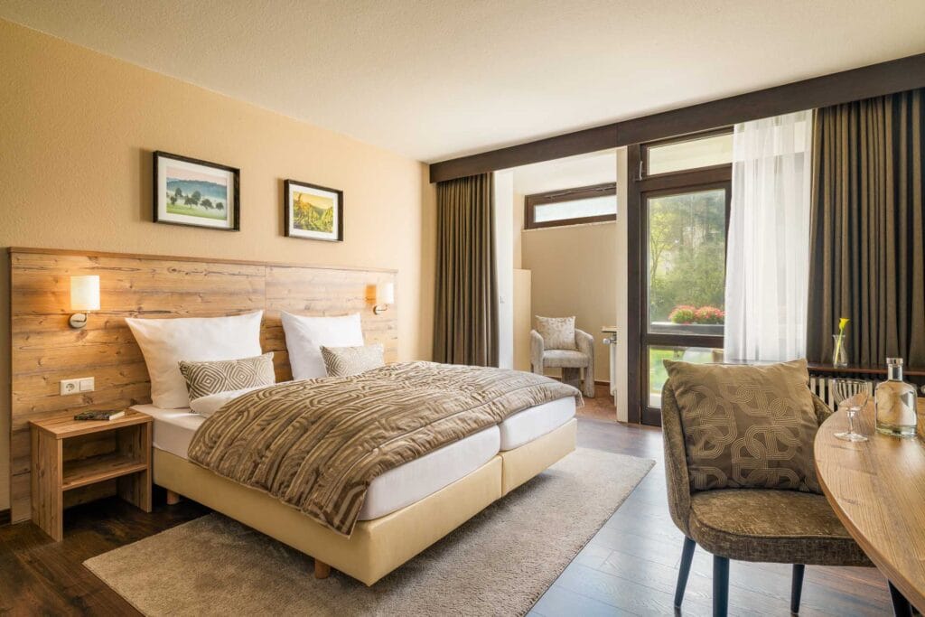 Komfortables Doppelzimmer mit Holzdekor, großen Fenstern und Naturblick im Hotel Luisenpark Bad Bergzabern