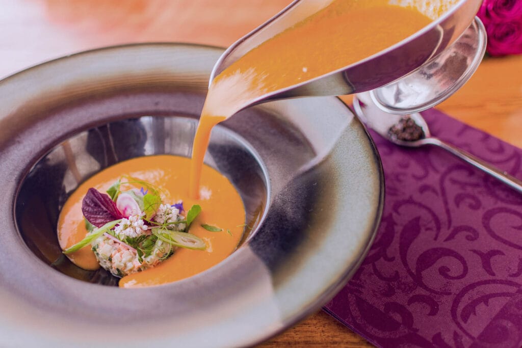 Gourmetsuppe mit Gemüsetatar und Blüten Feinschaumige Suppe wird in tiefem Teller über fein dekoriertes Gemüse gegossen.