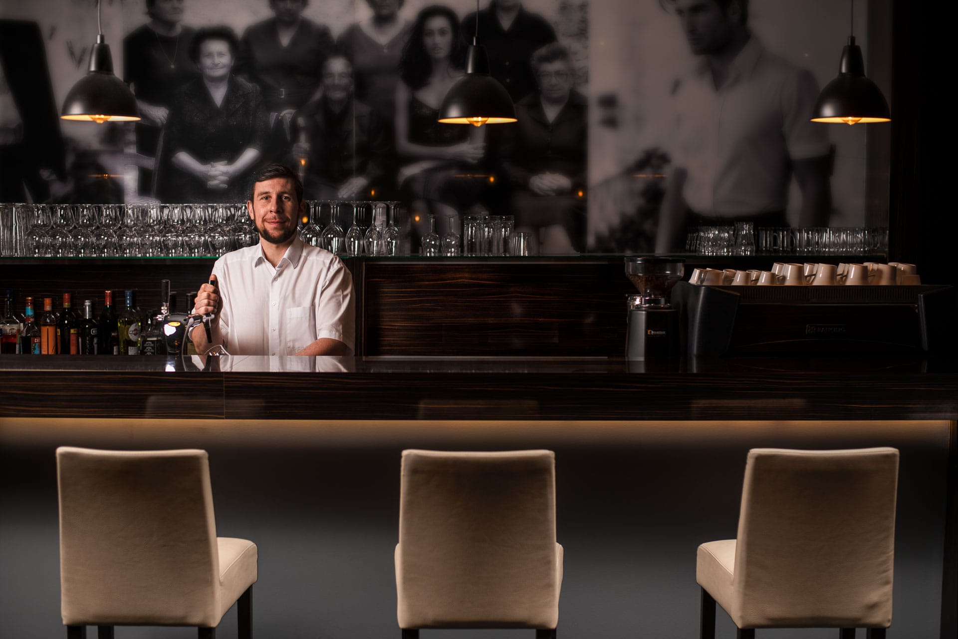 Hotelbar mit Barkeeper im Boutique Hotel Société in Baden-Baden, stilvoll beleuchtete Theke mit Glasregalen und Espresso-Maschine
