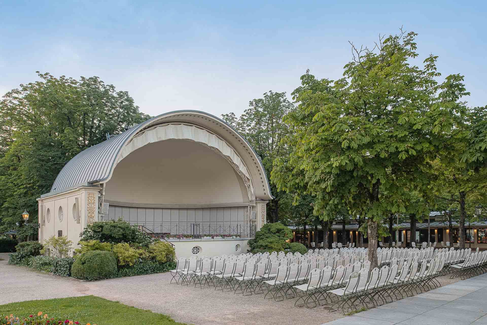 Weiße Konzertmuschel mit Stuhlreihen im Kurgarten von Baden-Baden, umgeben von Bäumen und Blumen
