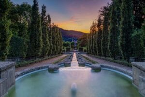 Langzeitbelichtung der Wasserspiele im Paradiesgarten Baden-Baden mit symmetrischer Baumreihe und Sonnenuntergang im Hintergrund